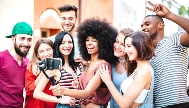 istock Multiracial friends taking selfie with mobile smart phone on stabilizer gimbal - Life style concept with milenial people having fun together sharing live feeds on social media channels - Bright filter 1383036135