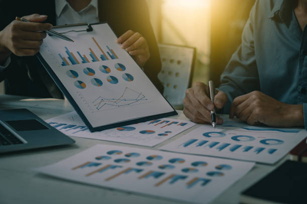 istock Two businessmen with pens pointing at financial market analysis charts using laptops while analyzing documents in hand with financial concept calculator. 1383039325