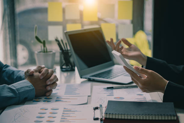istock Two businessmen with pens pointing at financial market analysis charts using laptops while analyzing documents in hand with financial concept calculator. 1383039350