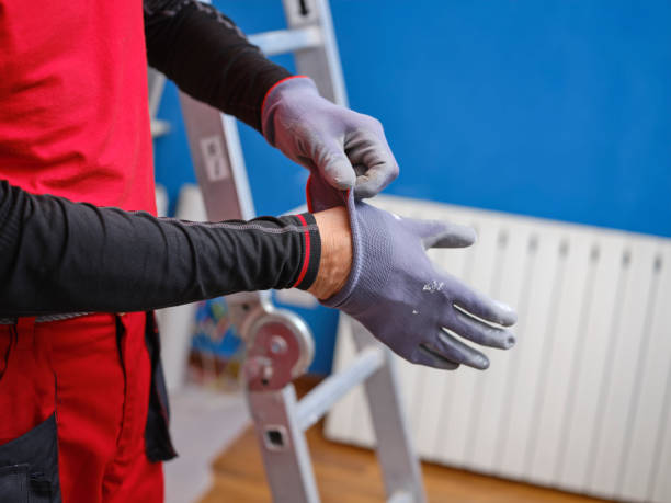 istock Craftsman while wearing protective work gloves ready to perform home renovation. Worker in work clothes on a construction site on an aluminum folding ladder in an apartment. 1383039761