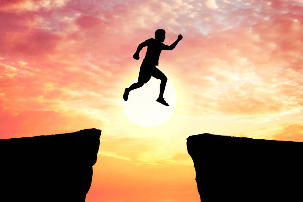 istock Silhouette young man jumping over precipice between two rocky mountains at sunset. 1383039835