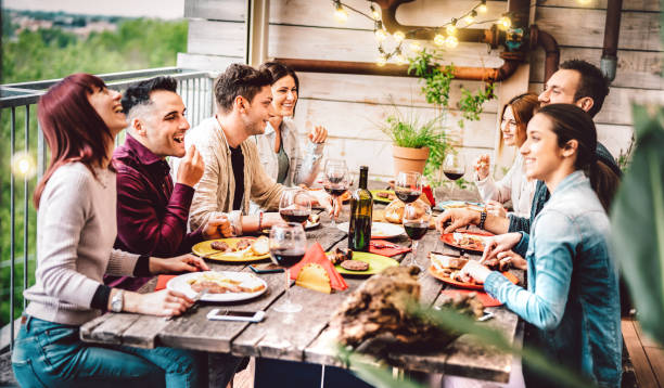 young friends dining and having fun drinking wine together on patio roof top supper party event - happy people eating bbq food at barbeque terrace - millenial life style concept on warm evening filter - picnic family barbecue social gathering imagens e fotografias de stock