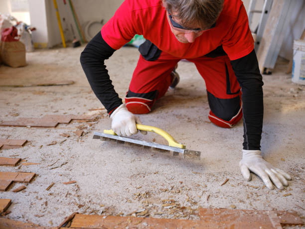 Craftsman in workwear who, using the rabot, removes excess glue left on the floor after removing the wooden parquet glued to the slab of an apartment. Worker at work while performing home renovation. artesano en ropa de trabajo que, utilizando el rabot, elimina el exceso de pegamento que queda en el suelo después de retirar el parquet de madera pegado a la losa de un apartamento. trabajador en el trabajo mientras realiza la renovación del hogar.