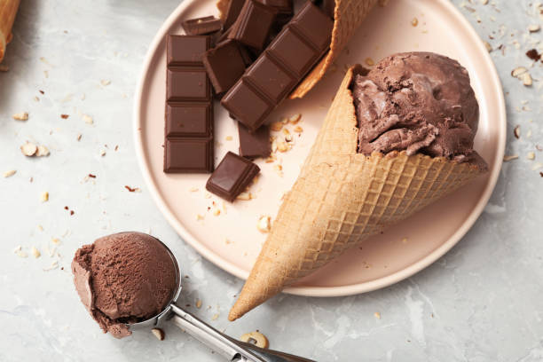 istock Delicious ice cream in wafer cone and chocolate pieces on light grey table, flat lay 1383046203