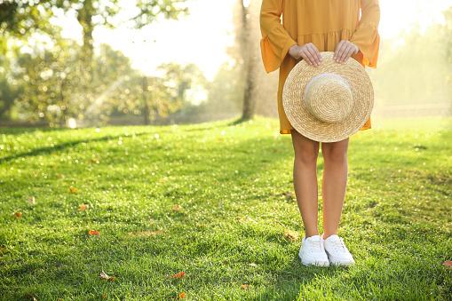 Woman wearing stylish yellow dress and sneakers with straw hat in park, closeup
