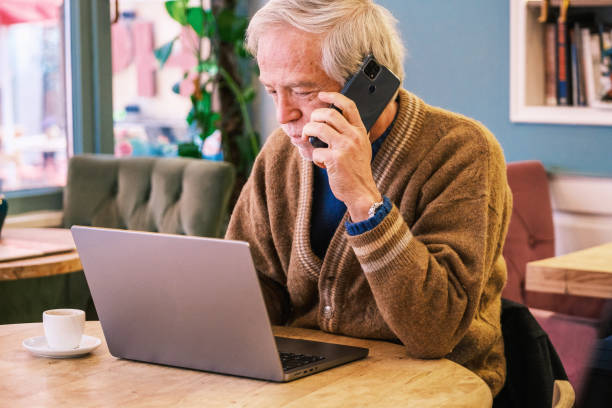 istock Senior man working on laptop and talking with phone at cafe 1383054038