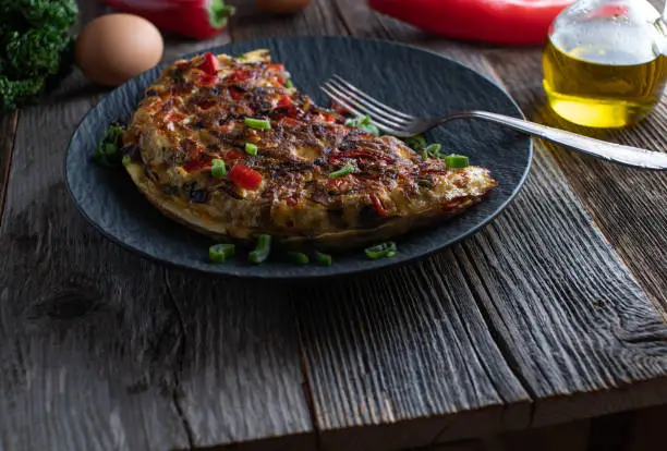 Delicious healthy mediterranean omelet or omelette. Served on a dark plate with old fashioned fork on rustic and wooden table background. Ready to eat