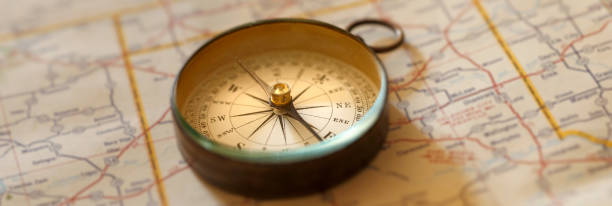 Compass On Road map A compass rests on top of a road map. Photographed with a very shallow depth o field. navigational compass photos stock pictures, royalty-free photos & images