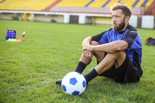 Soccer player sitting on a field. About 30 years old, Caucasian male.