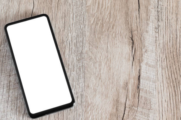 istock Mobile phone with white screen on wooden surface moke up. Smartphone shot flat lay on a table with a single-color screen. Copy space. 1383083889
