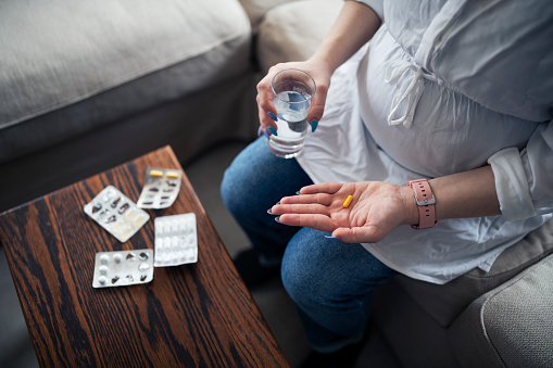 Pregnant woman taking supplement pill at home ,one hand holding pill and the other one holding a glass of water.
