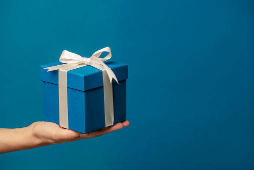 Woman giving gift box against blue background.