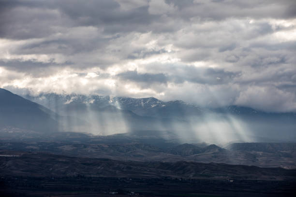 Dramatic sun light piercing through the clouds and hitting the mountains, in an epic scenery.