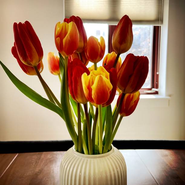 A bouquet of vibrant yellow and orange tulips is elegantly displayed on a table, brightening the indoor space with their cheerful colors during the spring season.