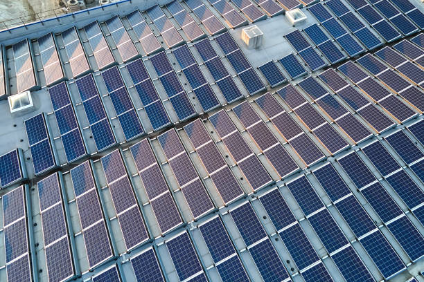 青い太陽光発電パネルを備えた太陽光発電所の空中写真を工業ビルの屋根に取り付け、グリーンエコエネルギーを生産しています。持続可能なエネルギー概念の作成 - インダストリアル音楽 ストックフォトと画像