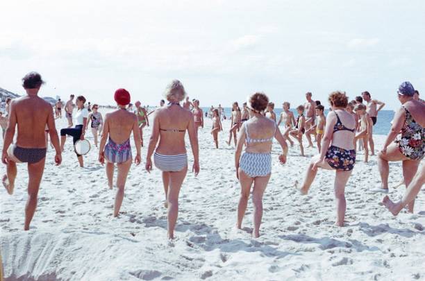 Westerland, Sylt, Schleswig Holstein, Germany, 1977. Summer vacationers have gathered on the beach for a gymnastics lesson. Also: gymnastics teacher with tambourine.