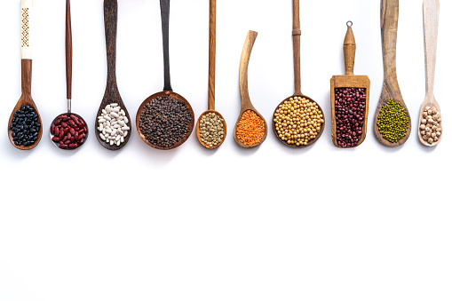 Assorted dried legumes on spoons ladle and serving scoop in a row isolated on white background copy space with beans, lentils, soybean and chickpeas