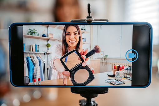 Pretty beauty vlogger recording make-up tutorial promoting product, social media marketing.