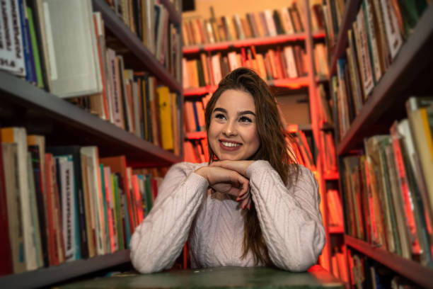 istock gorgeous beauty sitting in the library serious and reading a super book. 1383107220