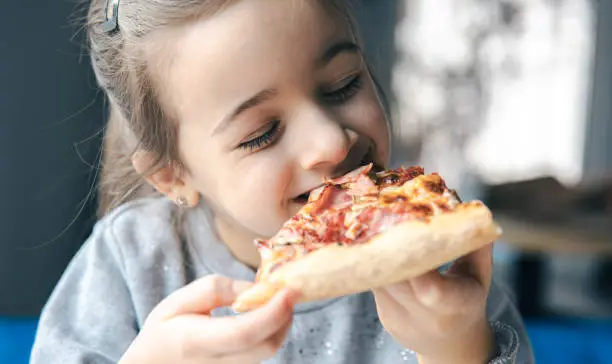 Photo of Portrait of a little girl with an appetizing piece of pizza.