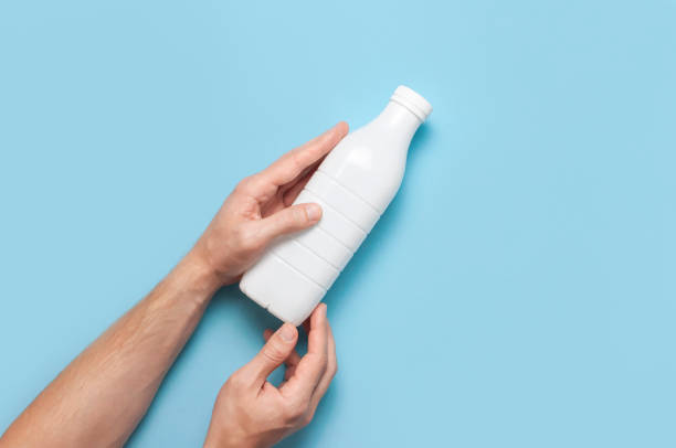 istock White plastic bottle containers for dairy products in male hands on blue background top view flat lay. Plastic Kefir Yogurt Milk Bottle. Packaging template mockup. Layout for your design 1383113659
