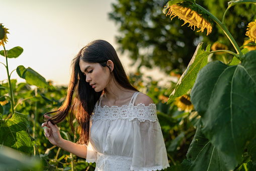 A portrait of a beautiful mixed-raced woman in a white dress at a sunflowers field during sunset.