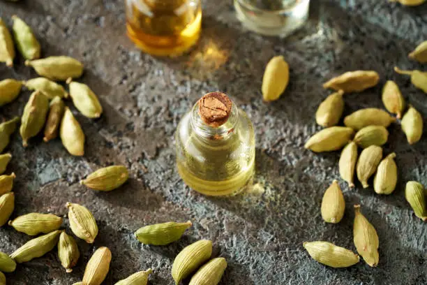 Essential oil bottle with cardamom seeds on a dark background