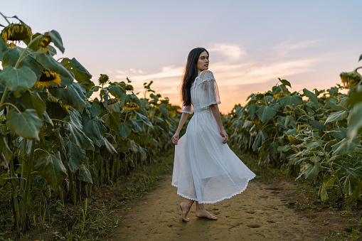 A portrait of a beautiful mixed-raced woman in a white dress at a sunflowers field during sunset.