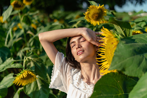 A portrait of a beautiful mixed-raced woman in a white dress at a sunflowers field during sunset.