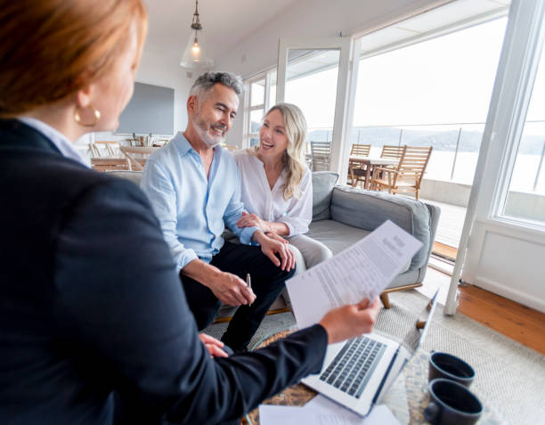 Happy mature couple meeting investments and financial advisor at home Happy mature couple meeting investments and financial advisor at home. They are happy and smiling sitting in the living room. The advisor is holding a document. There is a laptop on the table real estate broker stock pictures, royalty-free photos & images