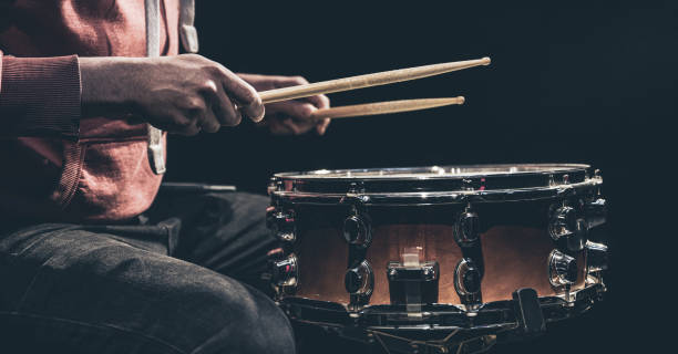 Snare drum and drummer's hands hitting drumsticks against a dark background. The percussionist plays with sticks on the floor tom on under studio lighting.. Concert and performance concept. drummer hands stock pictures, royalty-free photos & images