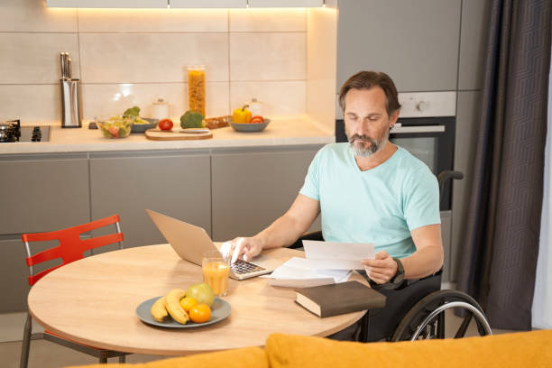 istock Adult man in a wheelchair working with documents in kitchen 1383120001