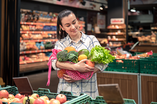 A woman holds a shopping bag with vegetables and fruits in a supermarket, grocery shopping, healthy food, healthy lifestyle.