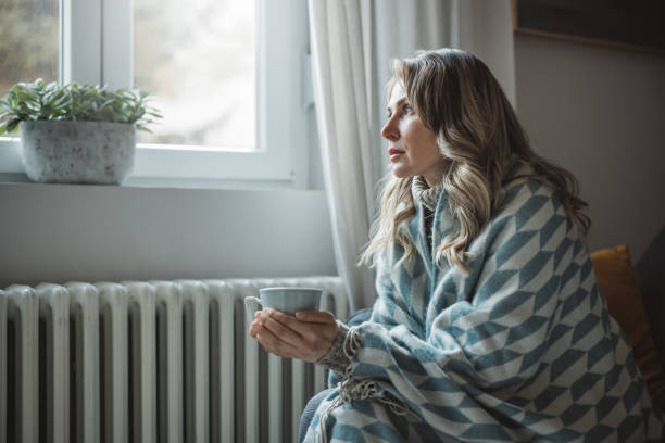 unwell woman feel cold in home with no heating - window home interior women people imagens e fotografias de stock