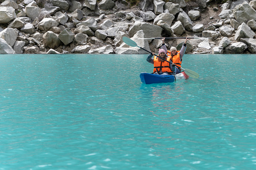 Two female friends paddling a kayak in a vivid turquoise water of Paron lagoon in Peru