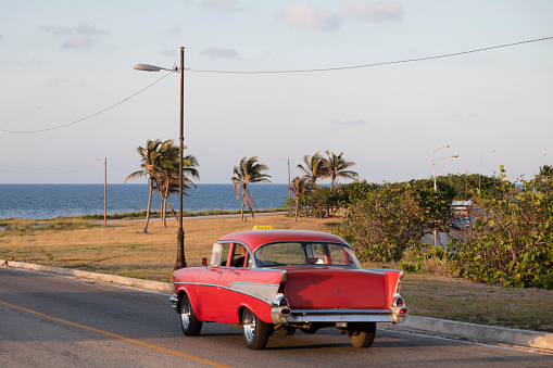 Red vintage American car driving along Gulf of Mexico coast towards Havana, Cuba