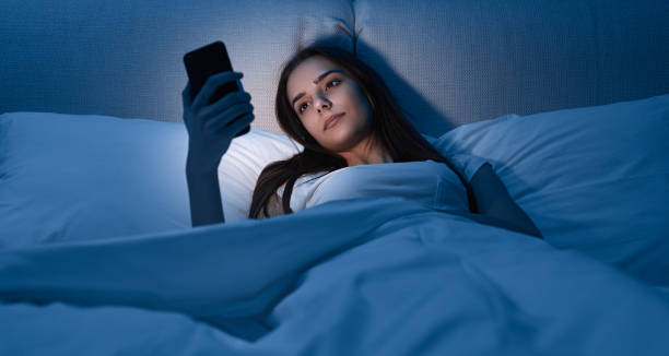 Young female with smartphone lying on bed stock photo