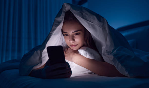 Young woman using smartphone in bed stock photo