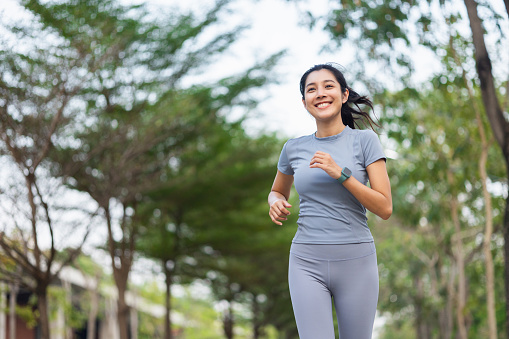 Happy slim woman wearing sportswear jogging in the city at sunrise. Young beautiful asian female in sports bra running outdoor. Workout exercise in the morning. Healthy and active lifestyle concept.