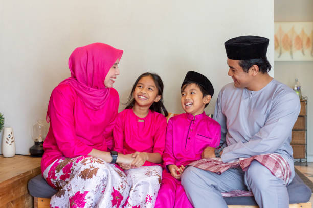 Lovely Family Celebrating Hari Raya Aidilfitri Eid-UL-FITR celebration - portrait of happy muslim family in traditional clothing sitting in living room and chatting hari raya singapore stock pictures, royalty-free photos & images