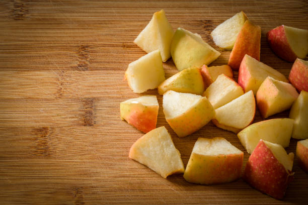 A pile of diced red apple. Pieces of apple sitting on the wooden chopping board.