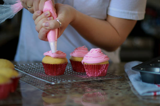 istock Woman spreading pink buttercream icing on vanilla muffins 1383236046