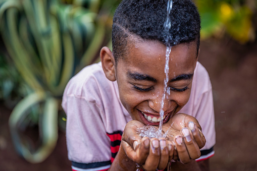 Happy African young boy drinking fresh water in village, Central Ethiopia. Potable water is very precious in Africa - women and children often walk long distances to bring back jugs of water that they carry on their back.