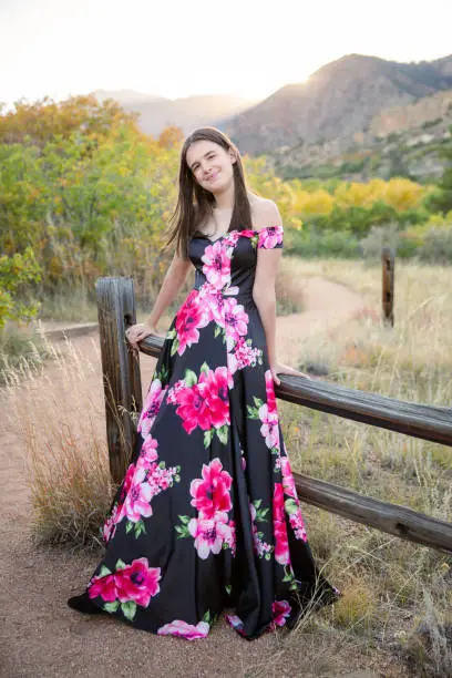 Beautiful girl in a long floral dress in autumn in the mountains smiling with fall colored leaves. Senior photos of a teen girl.