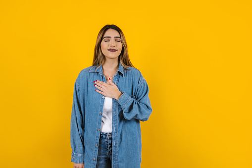 Young latin woman practicing breathing or breaths fresh air with closed eyes on yellow background in Mexico Latin America