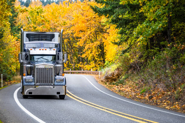 istock Powerful old style dark gray classic big rig semi truck with refrigerator unit on the front wall of the reefer semi trailer running on the winding mountain road through the autumn forest 1383299496