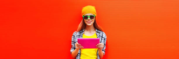 Portrait of stylish cool young woman model with tablet pc wearing colorful clothes on vivid background, blank copy space for advertising text stock photo