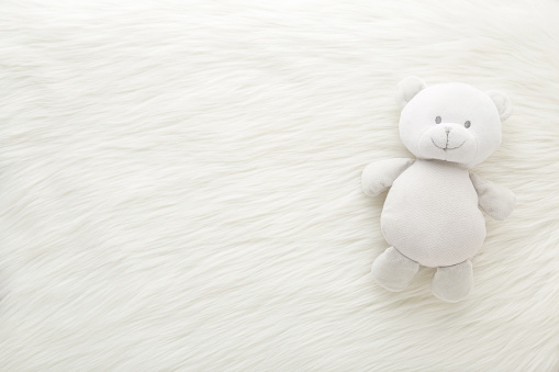 Smiling baby teddy bear on white fluffy fur blanket background. Closeup. Empty place for inspiration, emotional, sentimental text, quote or sayings. Top down view.