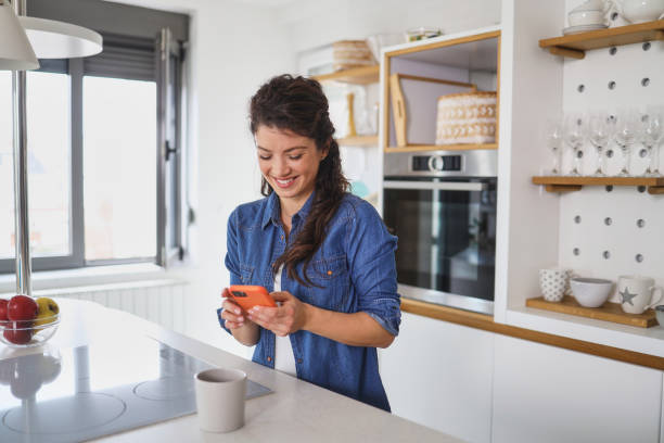 istock Smiling mature woman messaging while standing at her kitchen in the morning 1383327863