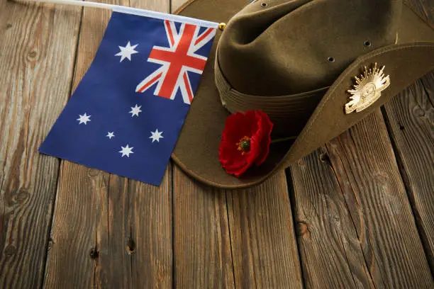 Anzac army slouch hat with Australian Flag and Poppy on wooden background.